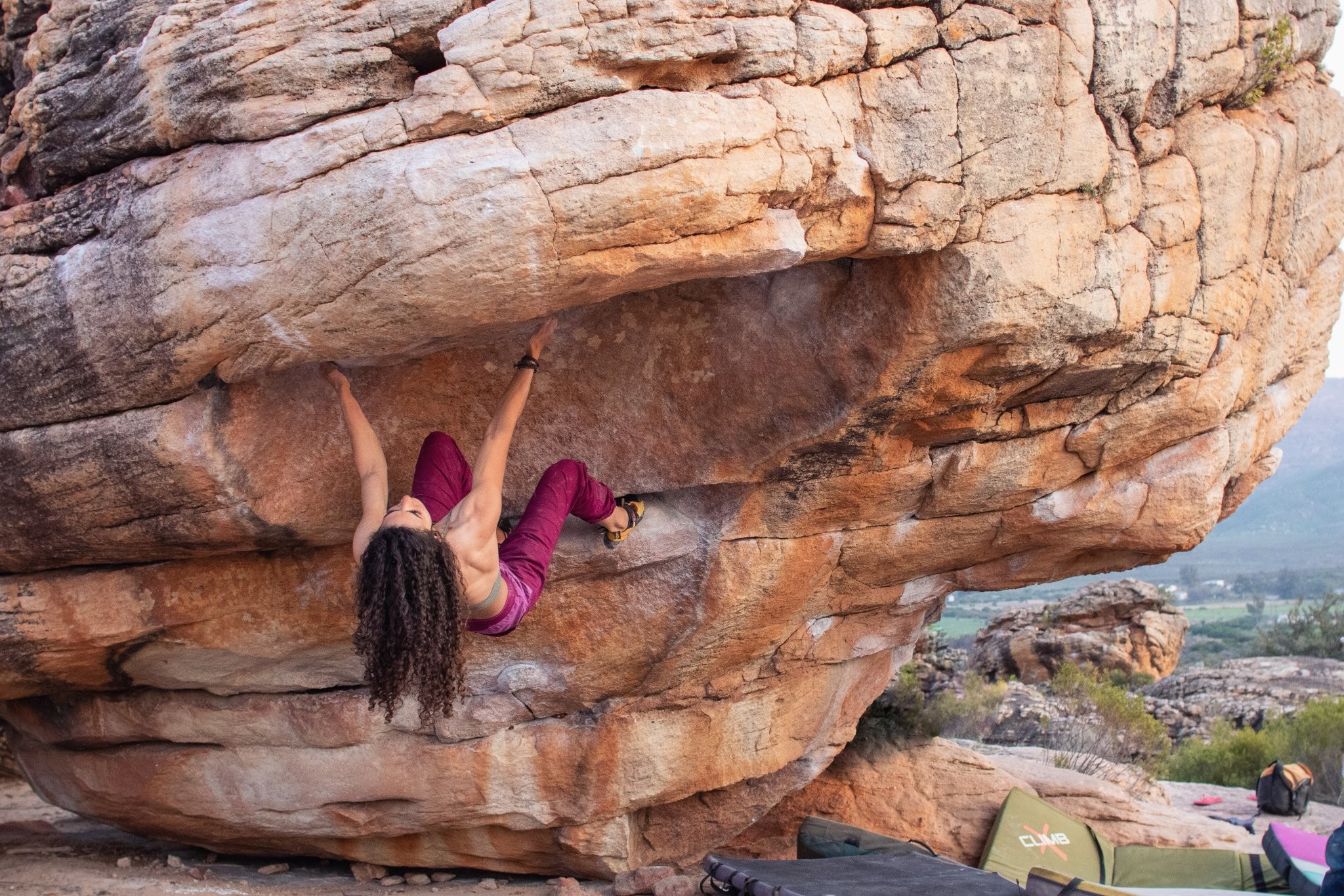 A female climber with long hair hanging from the underside of a rock face.