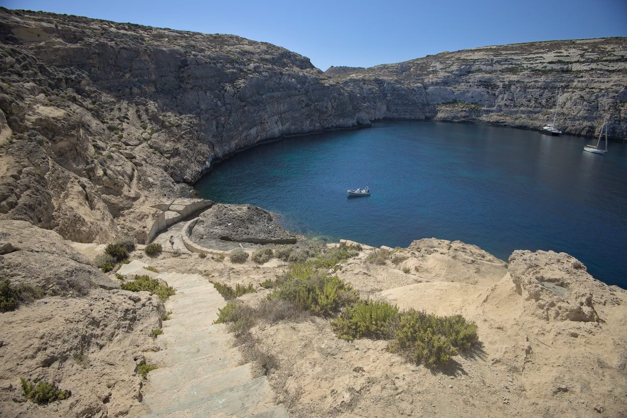 Escena de costa amb unes escales que condueixen a una petita cala de roca.