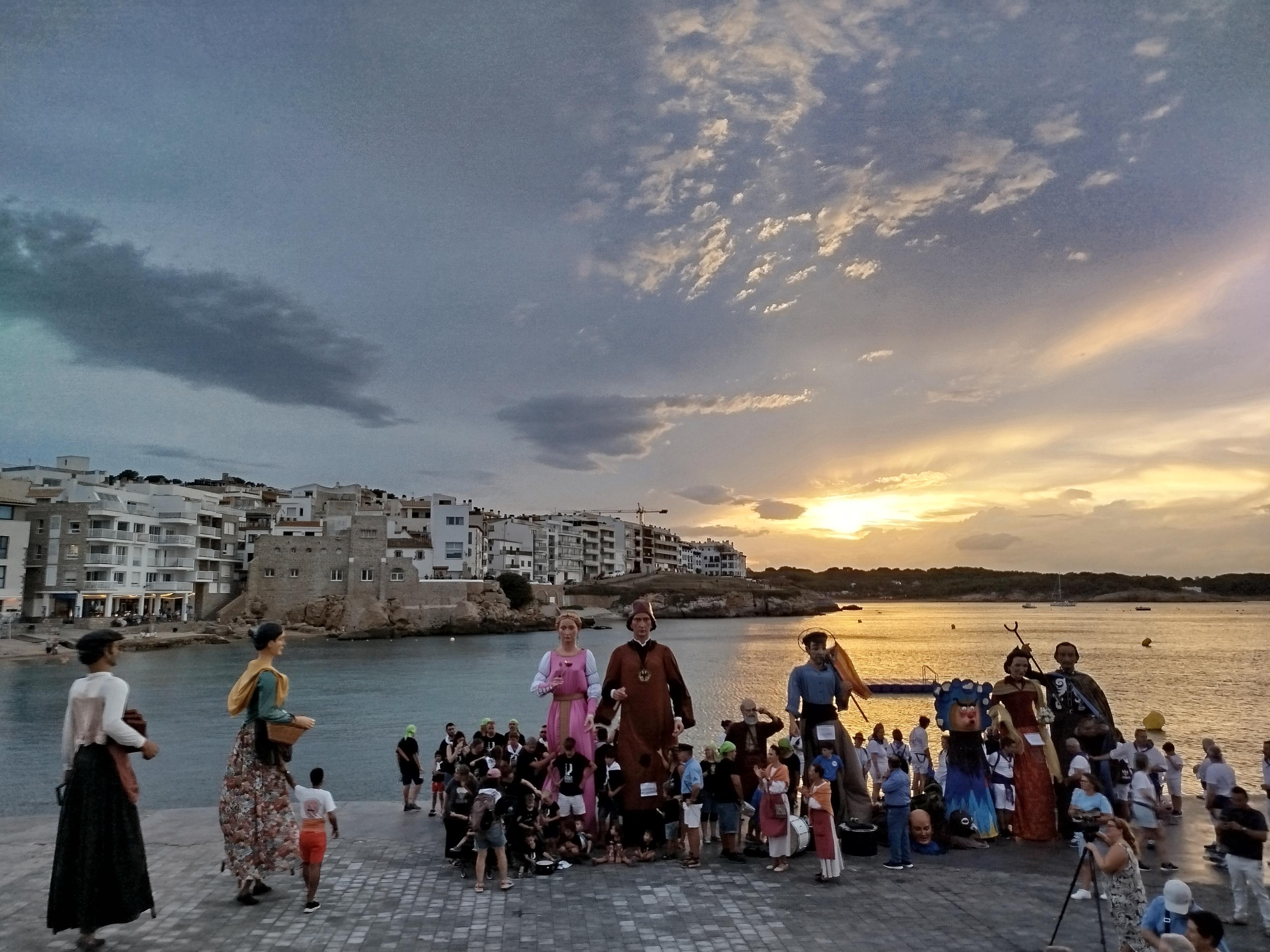 Erraldoi konpartsak L'Escalako Riban, itsasertzean. Atzean herriko etxe batzuk, itsasoa, Ampurieseko kostaldea eta arratseko zeru dramatikoa. Erraldoi konpartsak L'Escalako Riban, itsasertzean. Atzean herriko etxe batzuk, itsasoa, Ampurieseko kostaldea eta arratseko zeru dramatikoa.