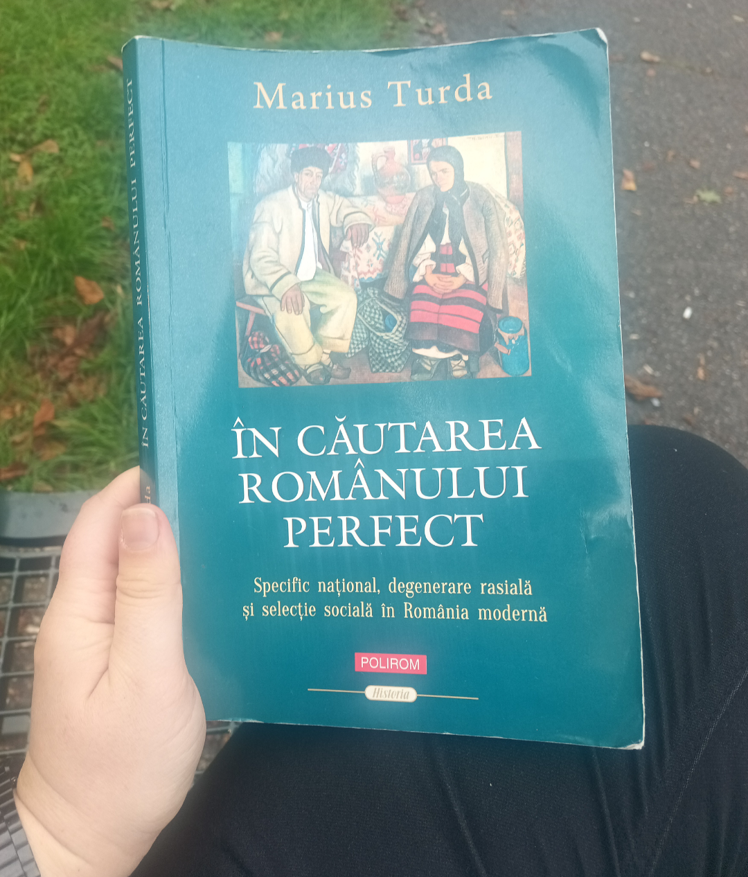Photo of a book held in the left hand, on a bench in the park. It has a blue cover and the title is in Romanian: In cautarea romanului perfect. Specific national, degenerare rasiala si selectie sociala in Romania moderna. The author is Marius Turda and the publishing company is Polirom. Photo of a book held in the left hand, on a bench in the park. It has a blue cover and the title is in Romanian: In cautarea romanului perfect. Specific national, degenerare rasiala si selectie sociala in Romania moderna. The author is Marius Turda and the publishing company is Polirom.
